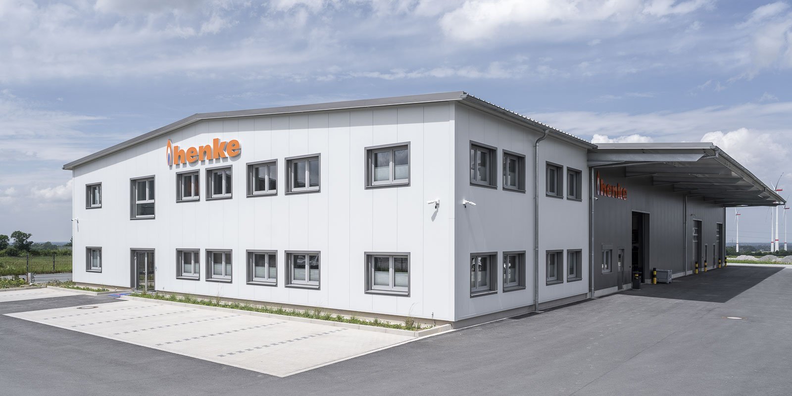 Ein modernes, zweigeschossiges Gebäude mit großen Fenstern und einem auffälligen orangefarbenen Schriftzug steht unter einem klaren Himmel.