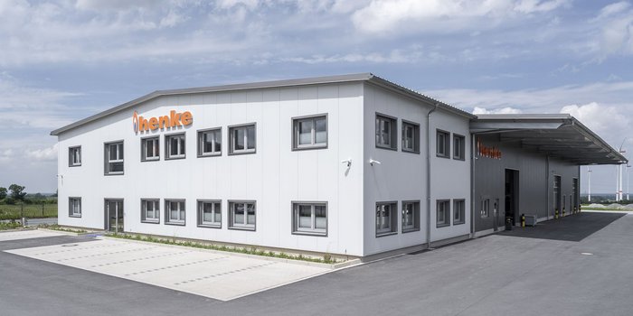 Ein modernes, zweigeschossiges Gebäude mit großen Fenstern und einem auffälligen orangefarbenen Schriftzug steht unter einem klaren Himmel.