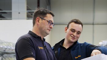 Zwei Männer in Arbeitskleidung betrachten gemeinsam Dokumente in einem modernen Lagerumfeld, beide wirken konzentriert.