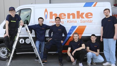Die Gruppe von Handwerkern zeigt sich vor einem Fahrzeug mit dem Logo 'henke', während sie eine Leiter benutzen.
