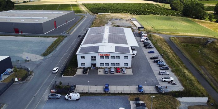 Die Ansicht eines Unternehmensgebäudes mit dem Namen 'henke', das von zahlreichen Autos und einer ruhigen Landschaft umgeben ist.