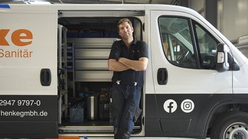 Ein Handwerker steht lässig an seinem weißen Lieferwagen, der mit Werkzeugen und Materialien für Sanitärarbeiten beladen ist.