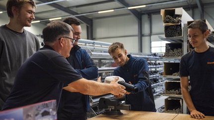 Fünf Männer diskutieren über Werkzeuge in einer Werkstatt Fünf Männer stehen um einen Tisch in einer Werkstatt und diskutieren über ein Werkzeug, das einer von ihnen hält.