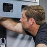 Ein Techniker arbeitet konzentriert an einem Gerät, während er seine Hand in einen engen Raum hineinführt.