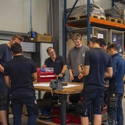 Eine Gruppe von Auszubildenden und einem Ausbilder arbeitet zusammen an einem Tisch, um praktische Fähigkeiten zu erlernen.