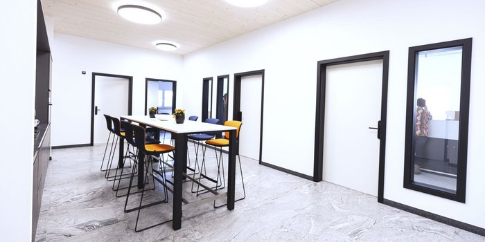 Ein moderner Büroraum mit einem langen Tisch, umgeben von Stühlen in verschiedenen Farben, und mehreren geschlossenen Türen.