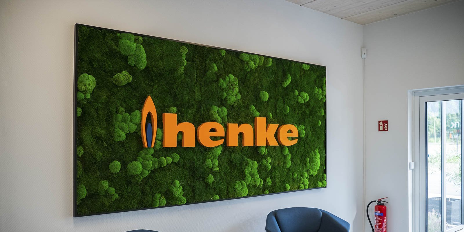 Die grüne Mooswand mit dem auffälligen Logo 'henke' schafft eine frische Atmosphäre in einem hellen Raum.