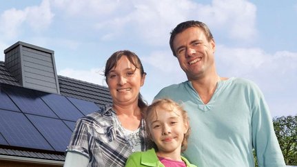 Eine kleine Familie, im Hintergrund ist ein Haus mit einer Photovoltaikanlage