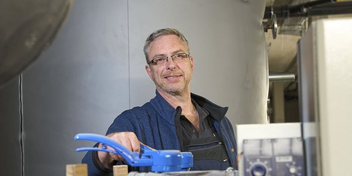 In einem technischen Raum steht ein lächelnder Mann, der ein blaues Gerät in der Hand hält und bereit ist zu arbeiten.