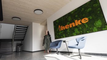Ein moderner Eingangsbereich mit einer grünen Mooswand und dem Schriftzug 'menke' in leuchtendem Orange, umgeben von stilvollen Möbeln.