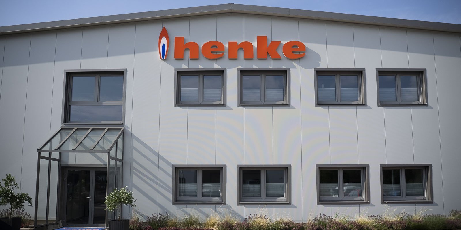Die moderne Fassade eines Unternehmensgebäudes mit dem auffälligen Schriftzug 'henke' in leuchtendem Orange.