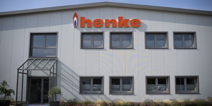 Die moderne Fassade eines Unternehmensgebäudes mit dem auffälligen Schriftzug 'henke' in leuchtendem Orange.