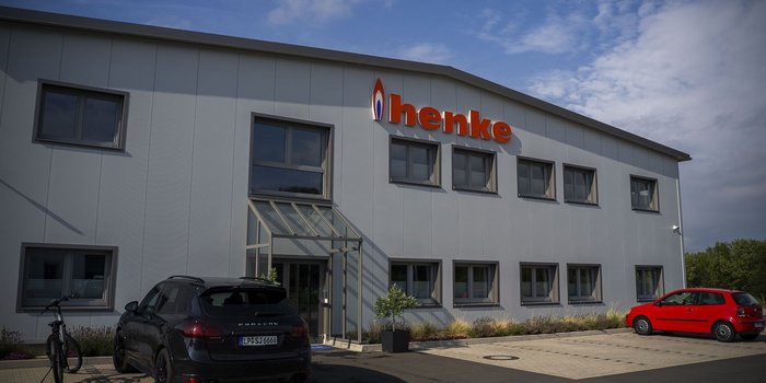 Ein modernes Firmengebäude mit dem Namen 'henke' in leuchtendem Orange, umgeben von einer gepflegten Landschaft.