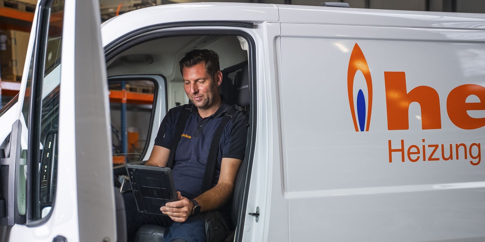 Der Techniker in Arbeitskleidung überprüft Informationen auf einem Tablet, während er im Lieferwagen sitzt.