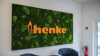 Ein modernes Wandbild mit dem Schriftzug 'henke' in leuchtendem Orange, umgeben von lebendigem, grünem Moos.
