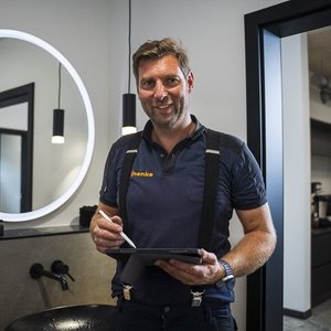 Ein fröhlicher Friseur steht in einem modernen Salon und hält ein Tablet in der Hand, bereit für den nächsten Kunden.